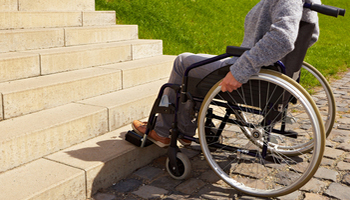 person on a wheelchair in front of steps with no ramp